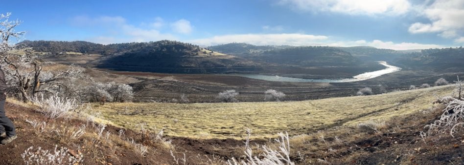 landscape with blue sky and white clouds over hills, a grass covered valley and a river running through it.